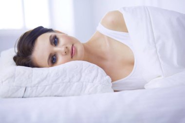 Güzel genç bir kadın beyaz yatakta yatıyor.