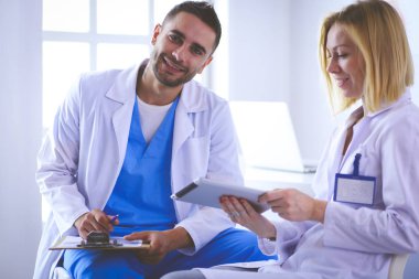 Yakışıklı doktor genç bayan hastasıyla konuşuyor ve ofisinde otururken notlar alıyor.