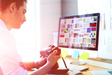 İnternette çalışırken bilgisayarın ve dizüstü bilgisayarın önünde grafik stüdyosunda oturan genç tasarımcının portresi.