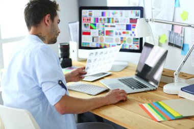 İnternette çalışırken bilgisayarın ve dizüstü bilgisayarın önünde grafik stüdyosunda oturan genç tasarımcının portresi.