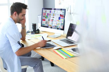 İnternette çalışırken bilgisayarın ve dizüstü bilgisayarın önünde grafik stüdyosunda oturan genç tasarımcının portresi.