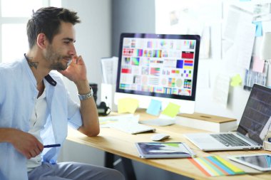 İnternette çalışırken bilgisayarın ve dizüstü bilgisayarın önünde grafik stüdyosunda oturan genç tasarımcının portresi.