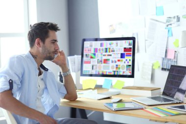 İnternette çalışırken bilgisayarın ve dizüstü bilgisayarın önünde grafik stüdyosunda oturan genç tasarımcının portresi.