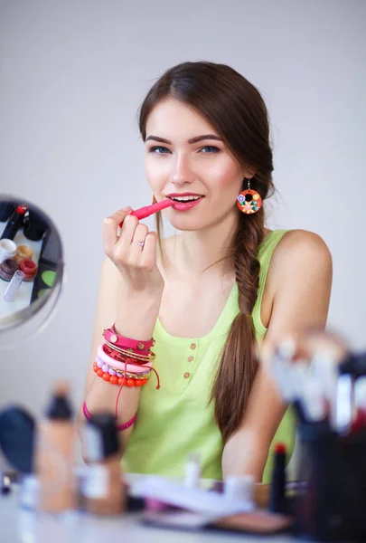 Joven hermosa mujer haciendo maquillaje cerca del espejo, sentado en el escritorio — Foto de Stock