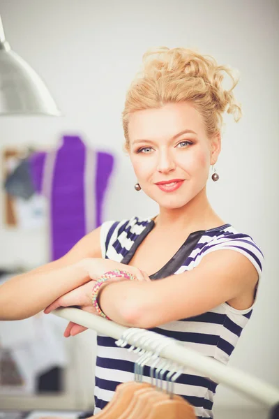 Beautiful young stylist near rack with hangers in office — Stock Photo, Image