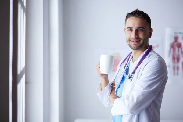 Young doctor with coffee cup in medical office — Stock Photo, Image