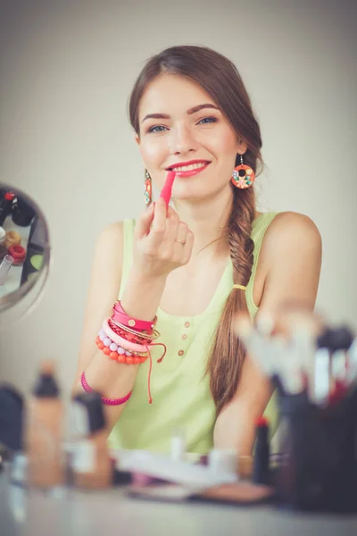 Joven hermosa mujer haciendo maquillaje cerca del espejo, sentado en el escritorio — Foto de Stock