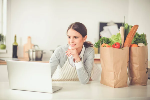 Smiling woman online shopping using computer and credit card in kitchen — Stock Photo, Image