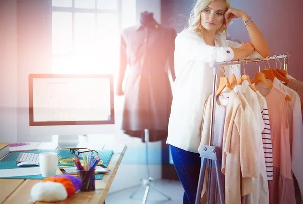 Beautiful young stylist near rack with hangers in office — Stock Photo, Image