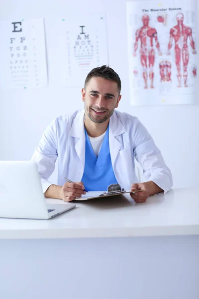 Retrato de um médico do sexo masculino com laptop sentado na mesa no consultório médico — Fotografia de Stock