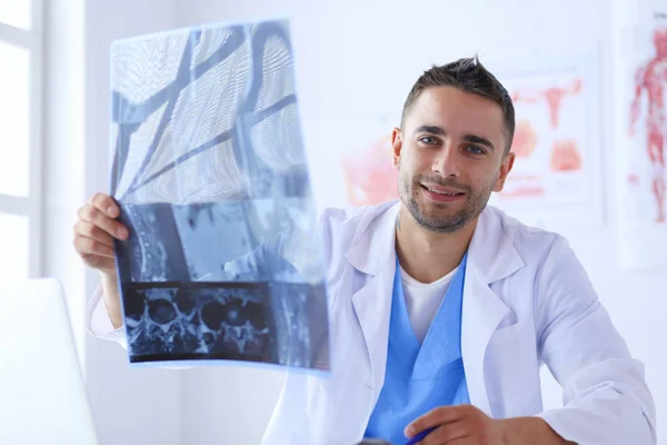 Junger Arzt sitzt an seinem Schreibtisch und analysiert ein Röntgenbild — Stockfoto