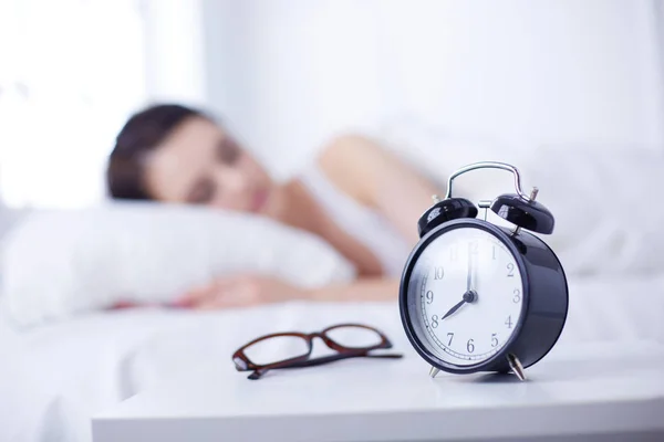 Frumoasă femeie tânără care doarme în timp ce stă în pat confortabil și fericit pe fundalul ceasului deșteptător — Fotografie, imagine de stoc