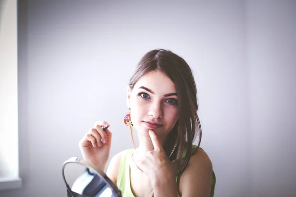 Joven hermosa mujer haciendo maquillaje cerca del espejo, sentado en el escritorio — Foto de Stock