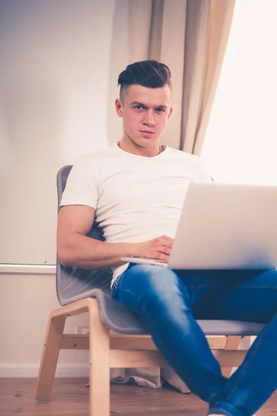 Młody mężczyzna siedzi na krześle z laptopa — Zdjęcie stockowe