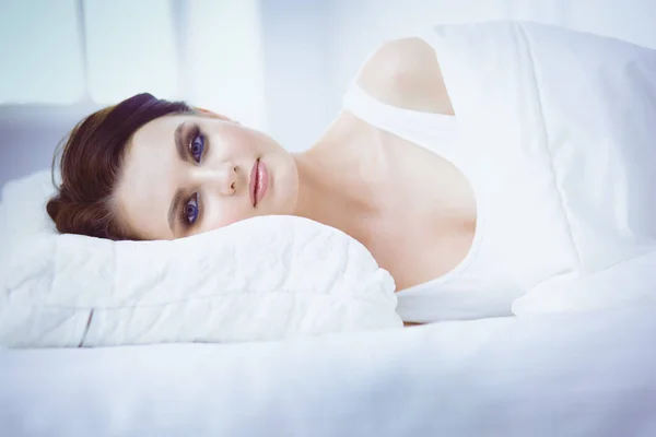 Όμορφη νεαρή γυναίκα ξαπλωμένη στο λευκό κρεβάτι — Φωτογραφία Αρχείου
