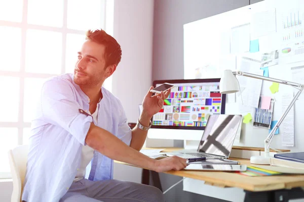 Portrait de jeune designer assis dans un studio graphique devant un ordinateur portable et un ordinateur tout en travaillant en ligne. — Photo