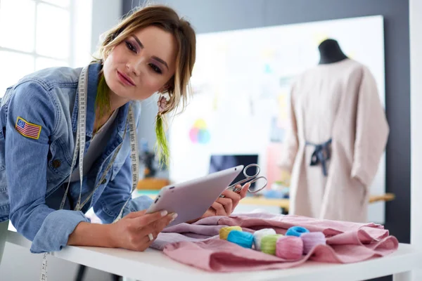 Mulher designer de moda trabalhando com ipad em seus projetos no estúdio — Fotografia de Stock