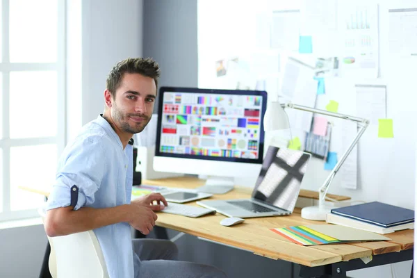 Portrait de jeune designer assis dans un studio graphique devant un ordinateur portable et un ordinateur tout en travaillant en ligne. — Photo