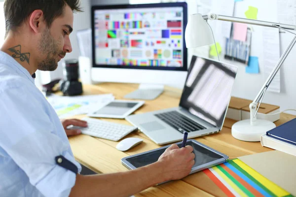 İnternette çalışırken bilgisayarın ve dizüstü bilgisayarın önünde grafik stüdyosunda oturan genç tasarımcının portresi.