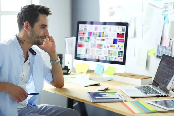 İnternette çalışırken bilgisayarın ve dizüstü bilgisayarın önünde grafik stüdyosunda oturan genç tasarımcının portresi.