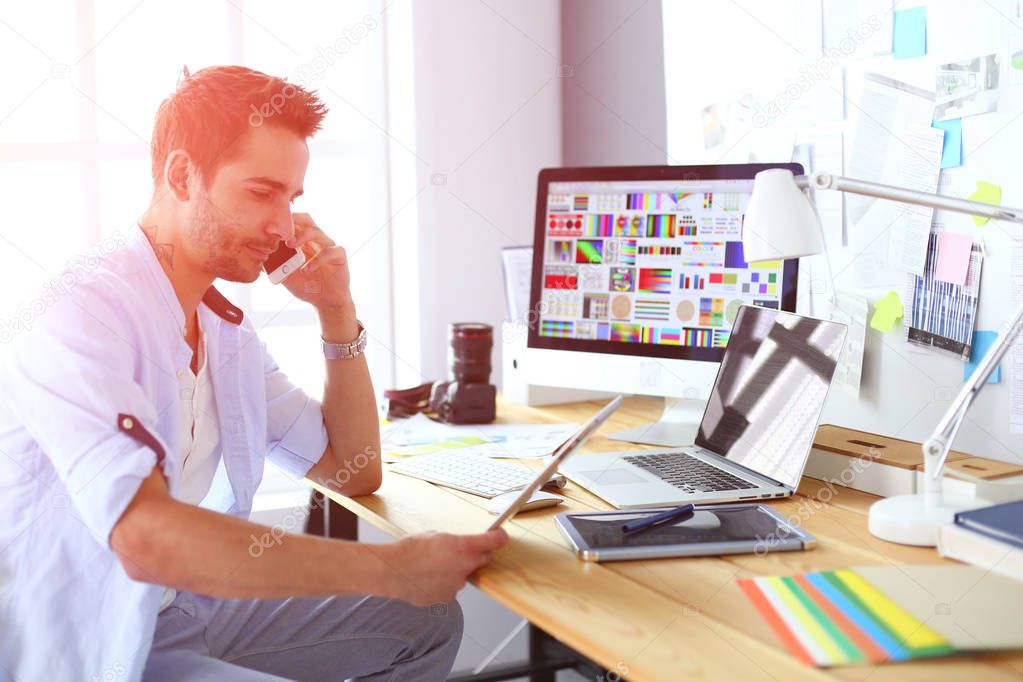 Portrait of young designer sitting at graphic studio in front of laptop and computer while working online.