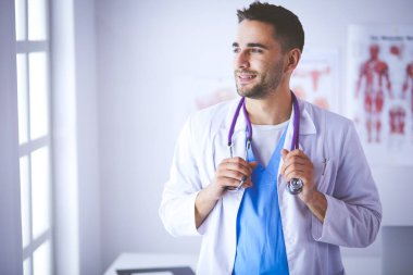 Genç ve kendinden emin erkek doktor portresi tıp ofisinde duruyor.