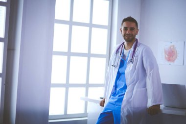 Genç ve kendinden emin erkek doktor portresi tıp ofisinde duruyor.