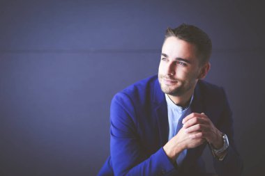 Gri arka planda yalnız oturan genç iş adamı