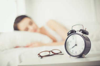Rahat yatakta yatarken ve blissfully çalar saat arka plan üzerinde uyuyan güzel genç kadın