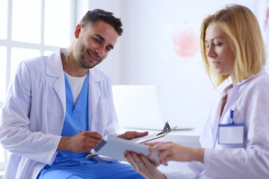 Yakışıklı doktor genç bayan hastasıyla konuşuyor ve ofisinde otururken notlar alıyor.