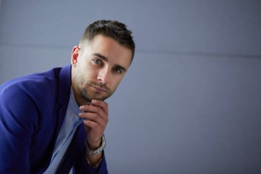 Gri arka planda yalnız oturan genç iş adamı