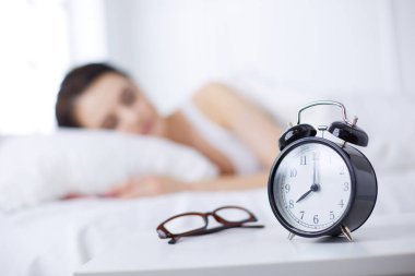 Rahat yatakta yatarken ve blissfully çalar saat arka plan üzerinde uyuyan güzel genç kadın