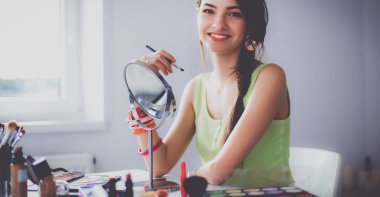 Genç ve güzel bir kadın aynanın yanında makyaj yapıyor.