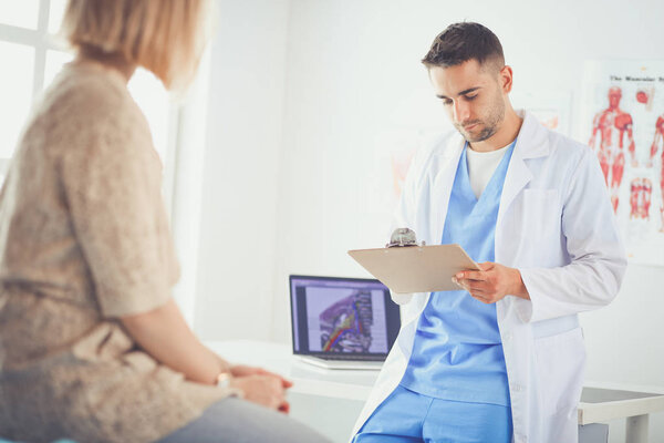 Красивый врач разговаривает с молодой пациенткой и делает заметки, сидя в своем кабинете
