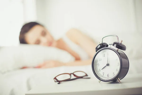 Beautiful young woman sleeping while lying in bed comfortably and blissfully on the background of alarm clock — Stock Photo, Image