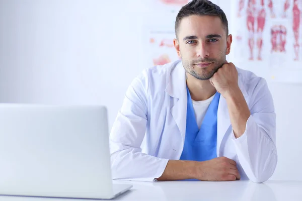 Ritratto di un medico di sesso maschile con computer portatile seduto alla scrivania nello studio medico — Foto Stock