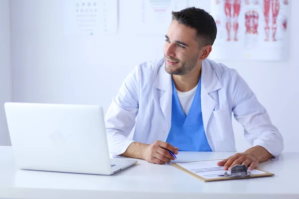 Портрет лікаря-чоловіка з ноутбуком, що сидить за столом у медичному кабінеті — стокове фото