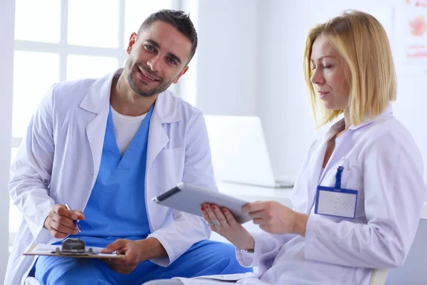 Schöner Arzt spricht mit junger Patientin und macht sich Notizen, während er in seinem Büro sitzt — Stockfoto