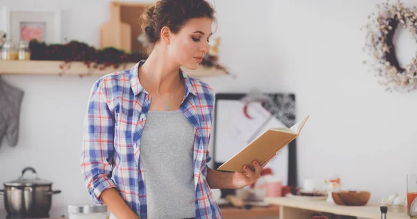 Mujer joven leyendo libro de cocina en la cocina, buscando receta — Foto de Stock