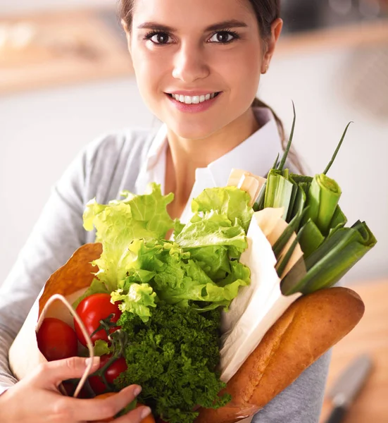 Молода жінка тримає продуктовий сумку з овочами стоїть на кухні — стокове фото