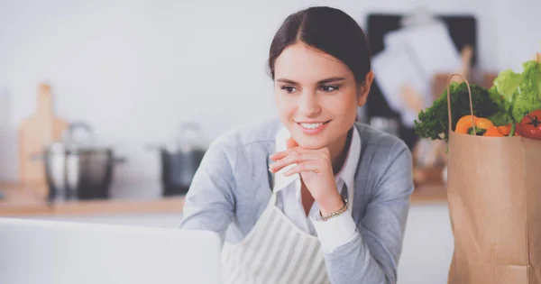 Vacker ung kvinna matlagning tittar på bärbar skärm med kvitto i köket — Stockfoto