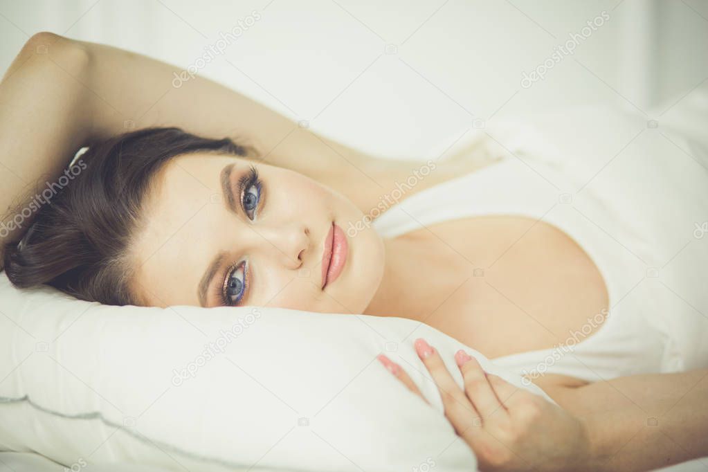 Beautiful young woman lying on white bed