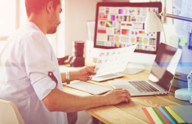 İnternette çalışırken bilgisayarın ve dizüstü bilgisayarın önünde grafik stüdyosunda oturan genç tasarımcının portresi