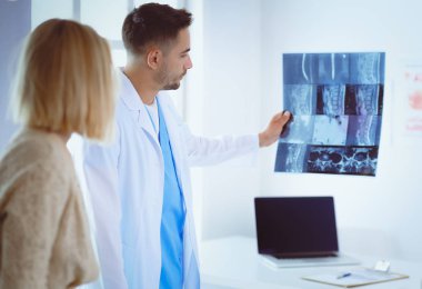Yakışıklı doktor genç bayan hastasıyla konuşuyor ve ofisinde otururken notlar alıyor.