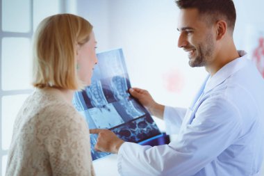 Yakışıklı doktor genç bayan hastasıyla konuşuyor ve ofisinde otururken notlar alıyor.