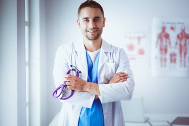 Genç ve kendinden emin erkek doktor portresi tıp ofisinde duruyor.