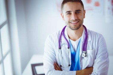 Genç ve kendinden emin erkek doktor portresi tıp ofisinde duruyor.