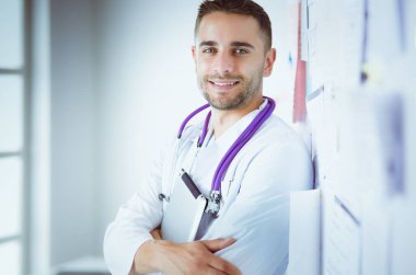 Genç ve kendinden emin erkek doktor portresi tıp ofisinde duruyor.