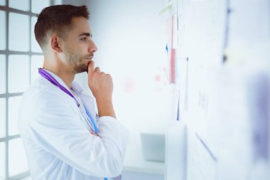 Genç ve kendinden emin erkek doktor portresi tıp ofisinde duruyor.