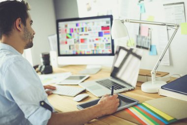 İnternette çalışırken bilgisayarın ve dizüstü bilgisayarın önünde grafik stüdyosunda oturan genç tasarımcının portresi